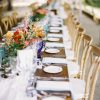 Long farm tables with white plates, florals, and vineyard chairs