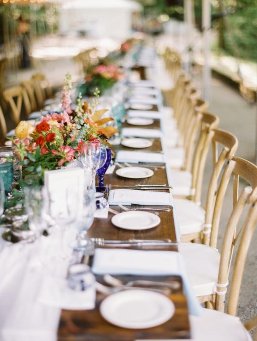 Long farm tables with white plates, florals, and vineyard chairs