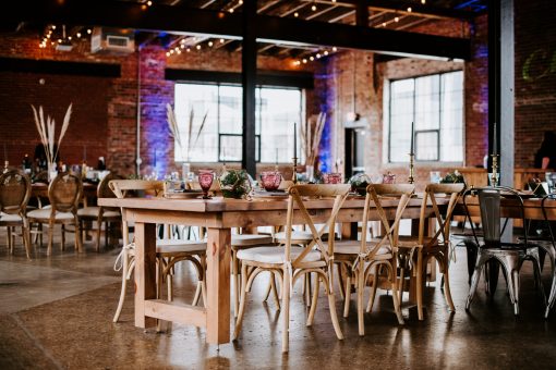 Wedding reception with farm table, cross back chairs, and table setting in an industrial venue.