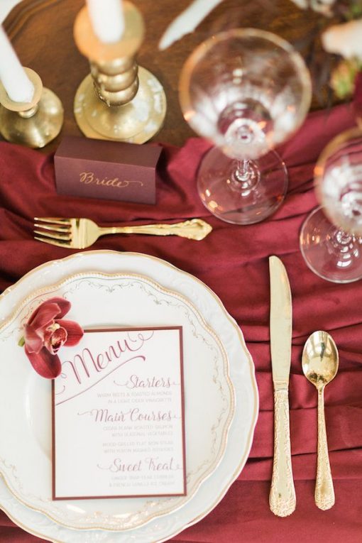 Gold and white china plates, gold flatware, vintage coups and brass candlesticks on a deep red drape