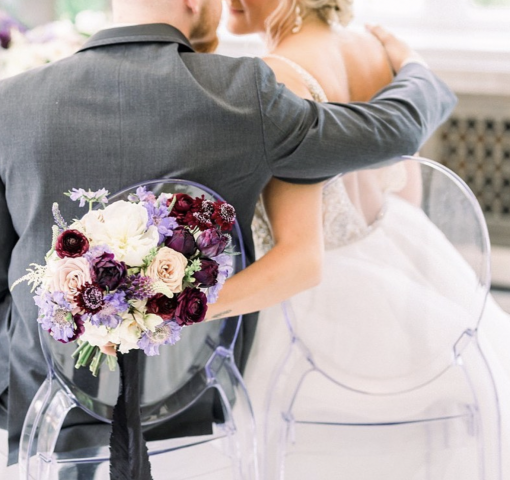 Couple with their backs to the camera sitting in clear chairs so you can see dress details