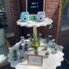 Two-tier off white scalloped table displaying cameras and plants at a baby shower