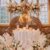 Photo of a sweetheart table with our double throne peacock chair rental, florals, and a lit sign with the couple's initials