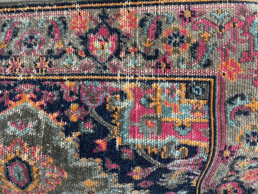 Close up of geometric designs that make up the corner of this rug. Colors are black, olive, hot pink, amber