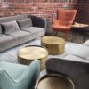 Lounge seating area at a corporate event with two modern gray sofas, an orange wingback arm chair, a seafoam green armchair and gold circular coffee tables