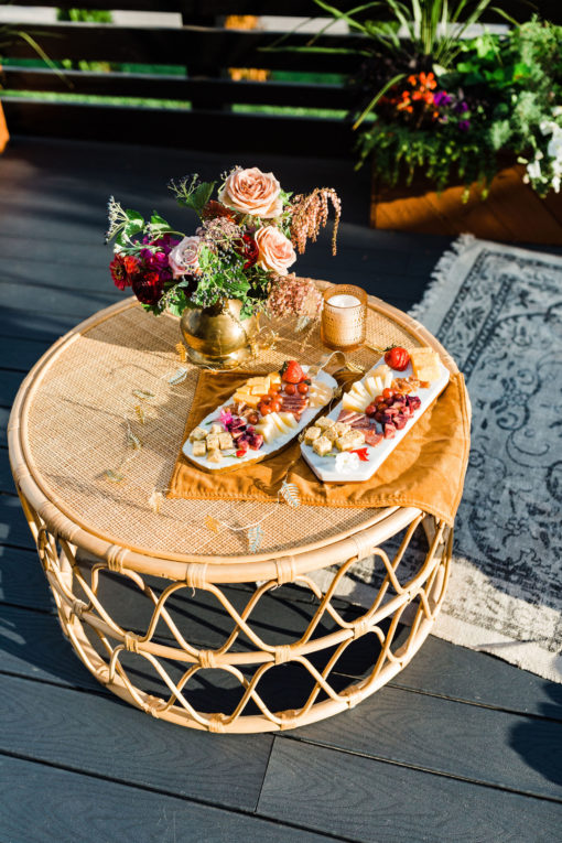 Top view of the Anay round rattan coffee table. Cheese and meat on marble trays and florals. Tori rug on the floor.