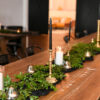 wooden farm table with greenery down the middle and votives and brass candlesticks