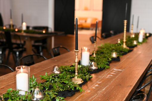 wooden farm table with greenery down the middle and votives and brass candlesticks