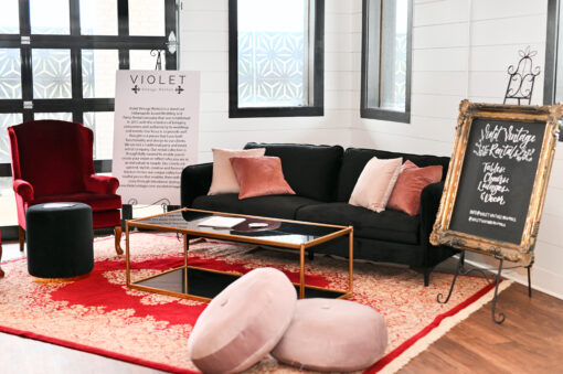 Lounge area rental with black sofa, deep red velvet high back armchair, black glass coffee table, and red vintage rug.
