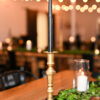 Brass gold candlestick with a black candle on a wood table with greenery