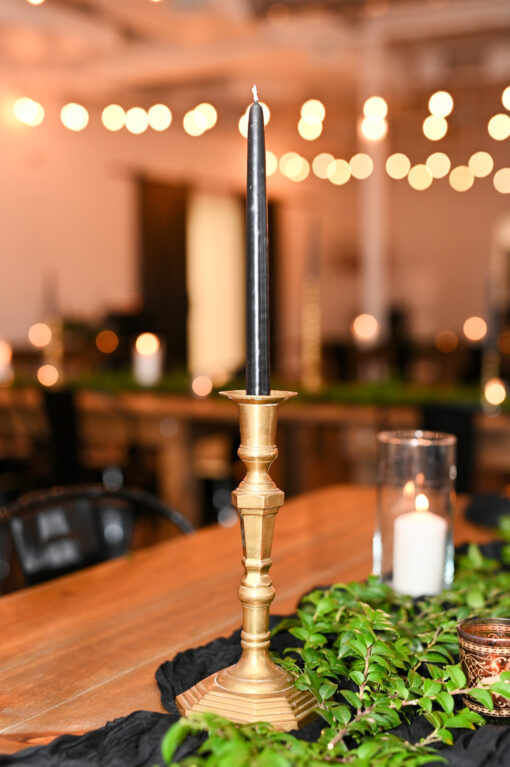 Brass gold candlestick with a black candle on a wood table with greenery