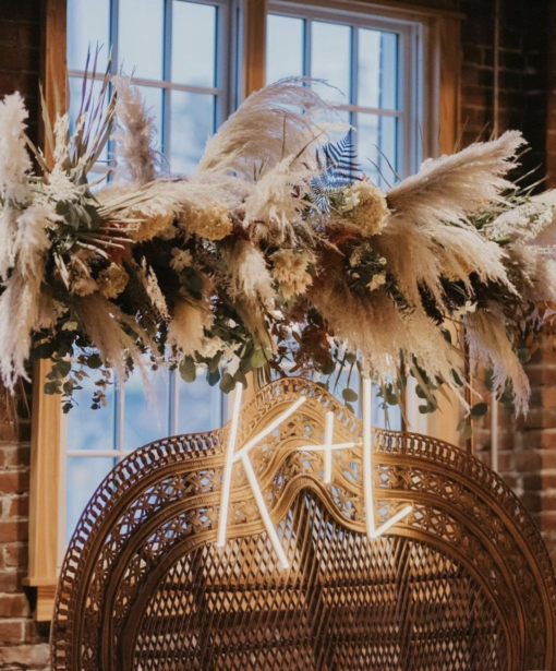 Close up on the back of the double throne peacock chair rental with neon initials K+L and florals hanging above