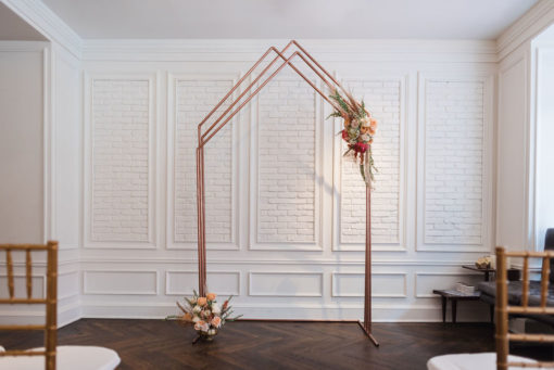 Colleen Copper Arch Backdrop used in wedding ceremony - chairs up front. Florals on arch.