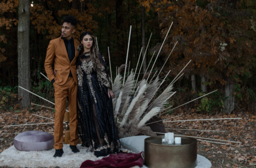 Moody photoshoot with a diverse couple standing on rugs with a gold coffee table and a dramatic backdrop.