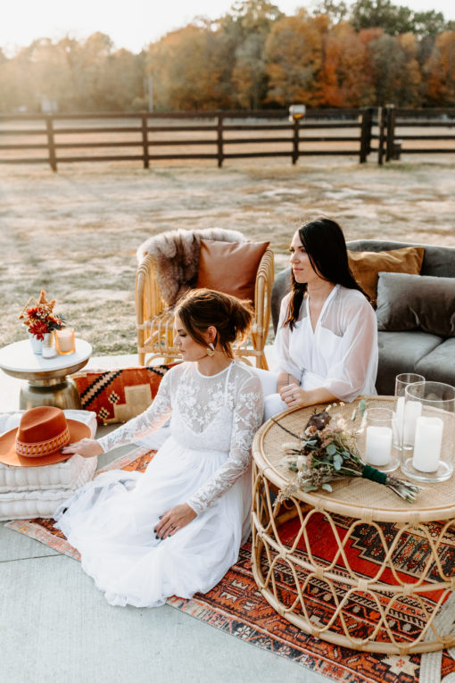 Wives in an outdoor photoshoot. Round coffee table in the foreground and gray sofa in the background.