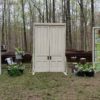 Entrance doors at an outdoor wedding ceremony. Doors are freestanding and closed. Two stain glass panels are to the side with church pews behind.