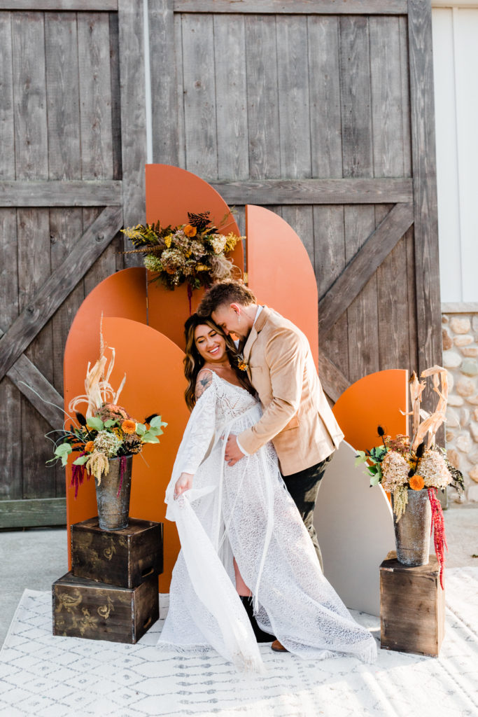 Couple posing for wedding photos in front of orange colored arched backdrop