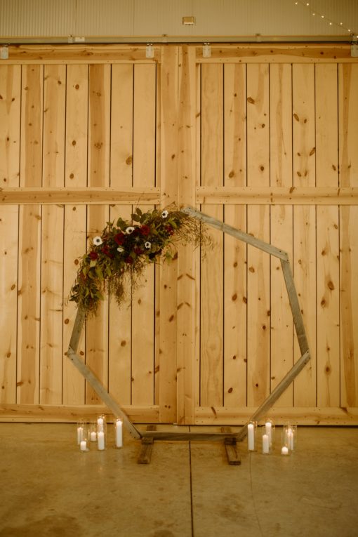 Tall open geometric arch with florals on top and candles near bottom as a wedding ceremony backdrop