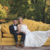 Outdoor photo shoot with husband and wife on a bold vintage yellow sofa sitting on a rug on grass. Trees in the background. Wedding portrait photo