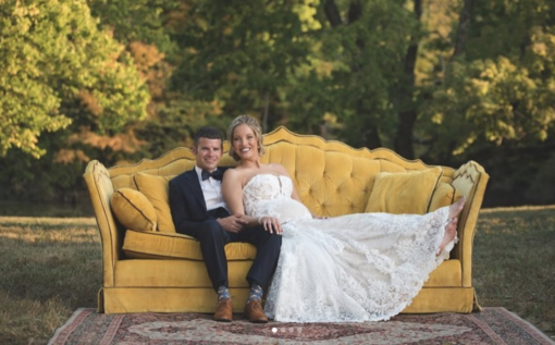 Outdoor photo shoot with husband and wife on a bold vintage yellow sofa sitting on a rug on grass. Trees in the background. Wedding portrait photo