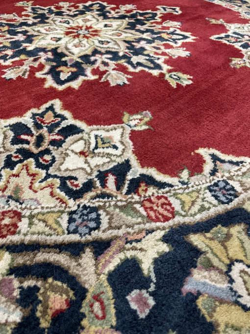 Close up of rug: navy and deep red background with lighter blue, green, cream ornate designs