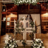 Elaborate carved gate doors used as a backdrop in a wedding ceremony. Florals drape the doors and the ground. Wedding held in a barn.