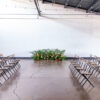 Folding wood and metal bistro chairs arranged in rows facing a middle aisle. Florals at the end again a wall