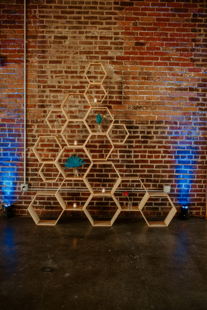 Honeycomb light wood backdrop with candles and flowers against a brick wall with blue lighting behind