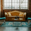 Yellow sofa, two blue chairs, a teal rug, glass round coffee table lit by a giant window.