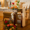 Side view of our wooden farm table used as a sweetheart table in a wedding reception. Florals at the feet and on the top. Loveseat in the back.