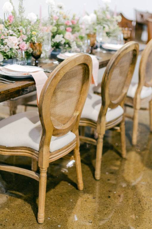 Cane backed wooden chairs at a wedding reception with dark wood farmtables.