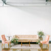 Pink modern velvet sofa in a lounge setting with pink chairs, on a rug with a wooden coffee table.