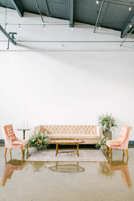 Pink modern velvet sofa in a lounge setting with pink chairs, on a rug with a wooden coffee table.