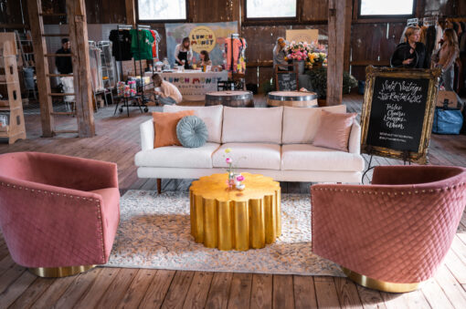White sofa, two pink barrel chairs and a gold coffee table in a seating area in a wooden barn.
