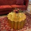 Red velvet couch on a rug patterned rug with a bright gold scalloped coffee table.