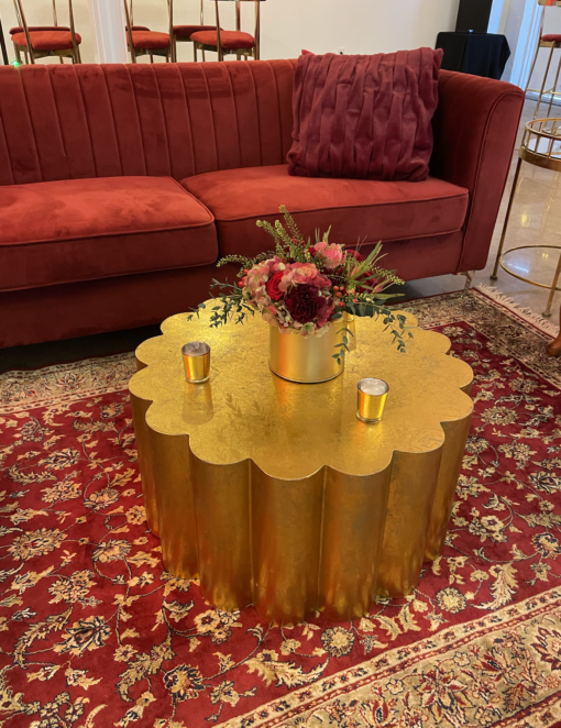 Red velvet couch on a rug patterned rug with a bright gold scalloped coffee table.