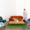 Burnt orange mid century mod sofa with side arm chairs in blue and green. Faux grass carpet under a wooden coffee table.