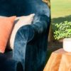 Close up of navy sofa with curved arm. Pink pillows. Wooden geometric side table with small plant in a white vase in a styled shoot outdoor lounge setting.