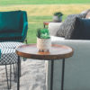Outdoor event with styled lounge set up. Side view - looking at the side of an off white sofa with black pillow decor. Wooden topped side table with black legs. Green velvet chairs.