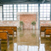 Industrial venue set up for wedding. Bank of windows up front with exposed brick wall. Pews set up for ceremony with aisle down the center.