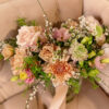 Close up of a corner of a blush colored velvet sofa with button tufts on back and seat. Pink florals displayed in the corner.