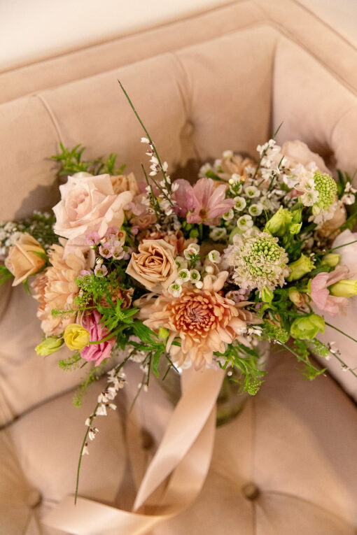 Close up of a corner of a blush colored velvet sofa with button tufts on back and seat. Pink florals displayed in the corner.