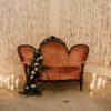 Pink victorian velvet loveseat draped with florals and surrounded by candles. White barn walls in the background