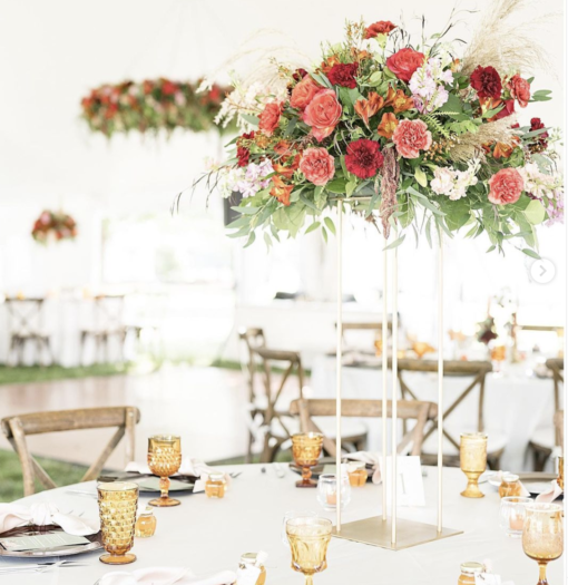 Outdoor wedding inside a tent. Round table at the reception with x-back chairs and tall florals in the center of the table. Amber mismatched goblets bring a pop of color.