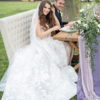 A young couple sitting on the settee at a wedding sweetheart table. On the grass, tree in background.