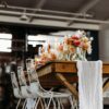 Wedding reception setup with farmtable and white wire chairs. White drape on the table with florals.