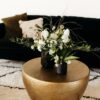 Gold round accent table with florals. Sitting on a black and white rug with a black sofa in the background