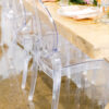 Clear acrylic chairs at a light wood farm table with bright orange and pink tablescape.