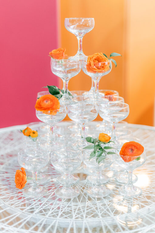 Vintage coupes used in a tower. Decorated with orange flowers. Top of vintage MCM table with white design and a glass top.