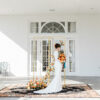 Bride standing on a large ornate rug with a gold backdrop posing for wedding photos